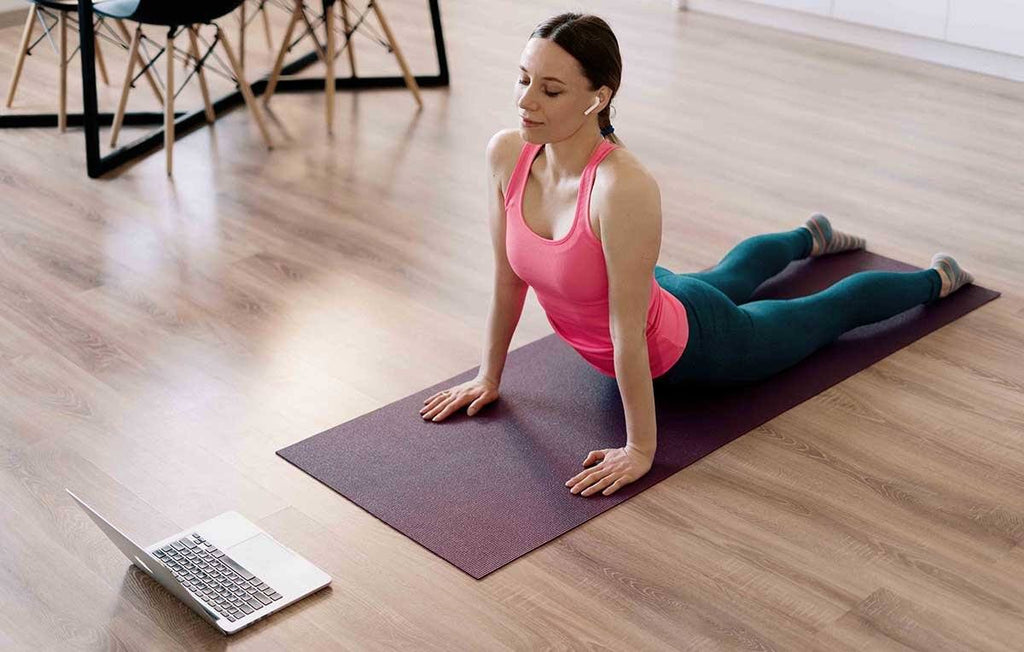 mulher fazendo yoga em casa através de aplicativo de yoga no notebook