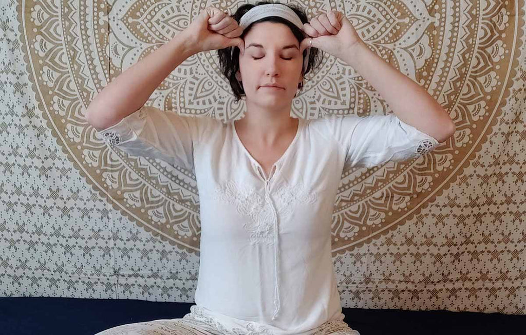mulher de olhos fechados usando roupas brancas tocando na cabeça fazendo kundalini yoga