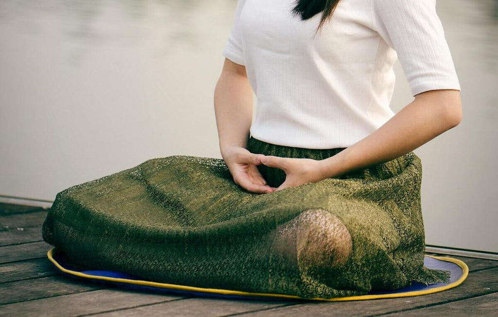mulher em posição de lótus à beira do lago fazendo meditação budista