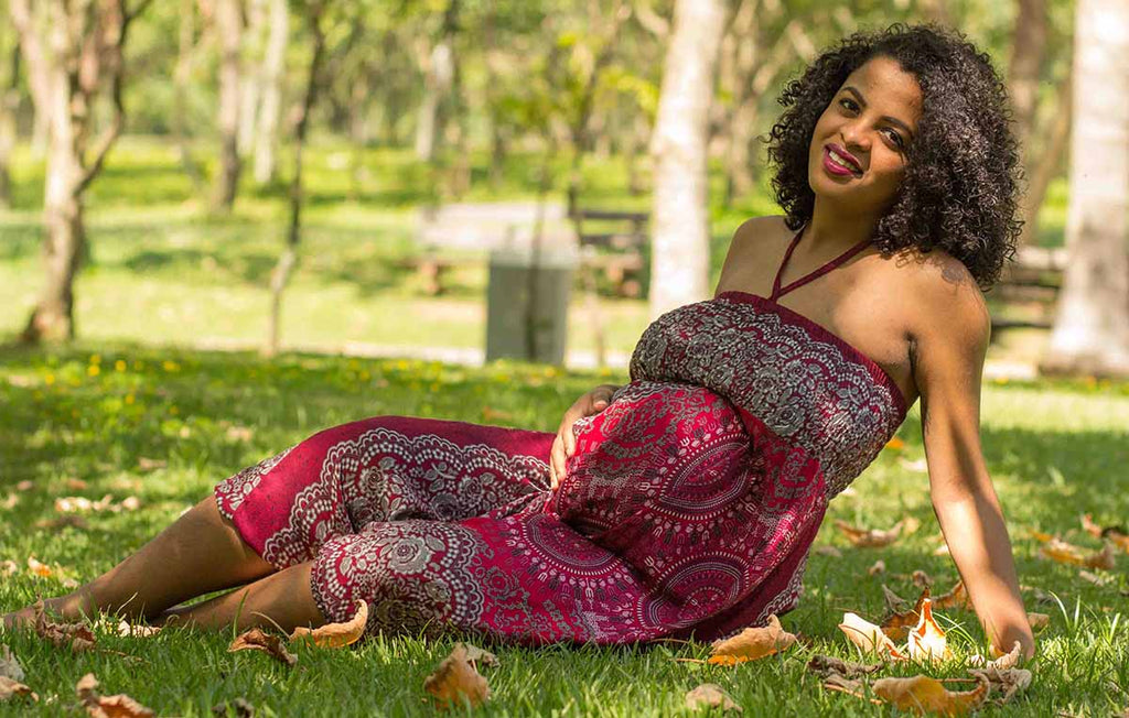 mulher grávida sentada na grama usando macacão calça harém para gestante