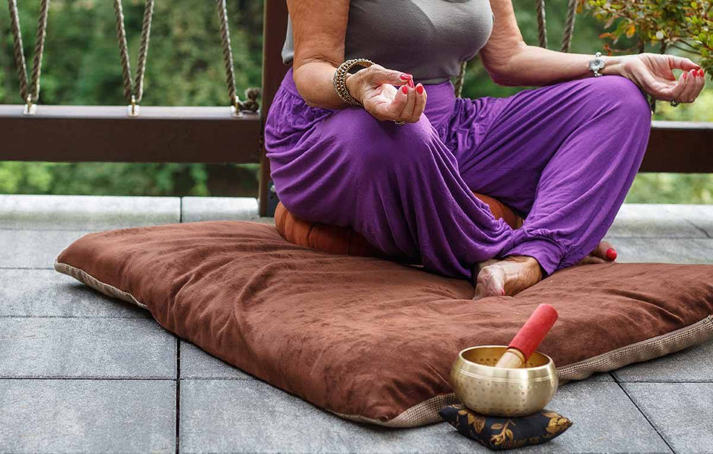 mulher madura sentada em almofada na sacada de casa praticando meditação transcendental