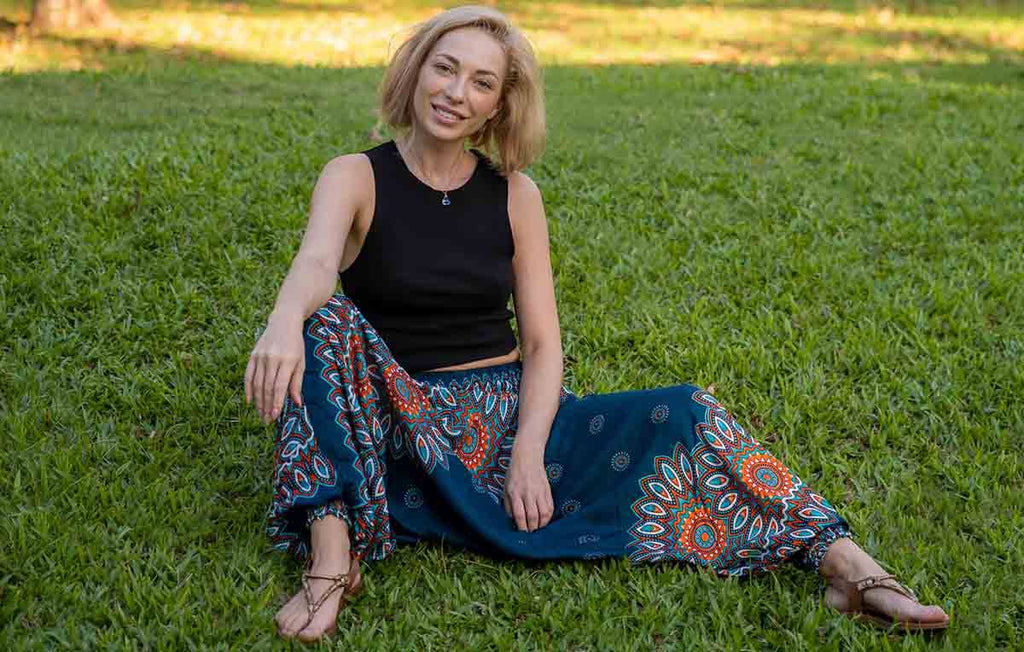 mulher sorrindo sentada na grama usando top preto e calça hippie saruel